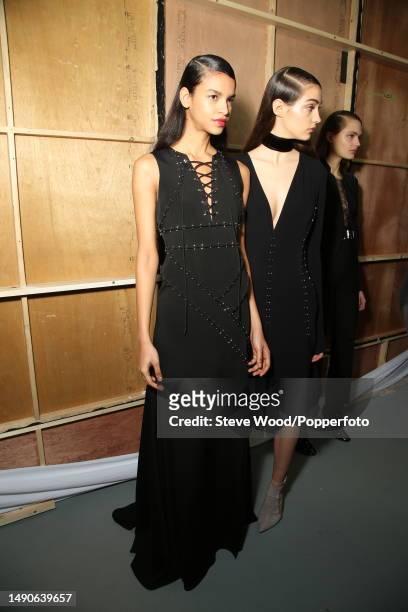 Backstage at the Antonio Berardi show during London Fashion Week Autumn/Winter 2016/17, models wear black crepe dresses featuring silver eyelets and...