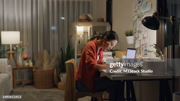 young asian woman use mask sheet on face sit front of desk with computer laptop and think create on work idea in living room at house at night. work from home. - authors night stockfoto's en -beelden