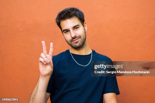 latino man looking at the camera and giving the peace sign - victory sign stock-fotos und bilder