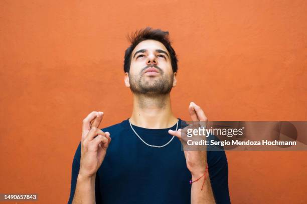 latino man looking up and crossing his fingers in hope, wishing - anticipation excited stock pictures, royalty-free photos & images