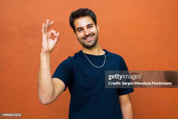 latino man looking at the camera and giving the ok sign smiling - guy with attitude mid shot stock pictures, royalty-free photos & images