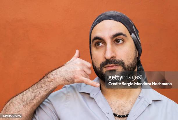 middle eastern, latino man with a bandana making a call me on the phone hand gesture - belt stockfoto's en -beelden