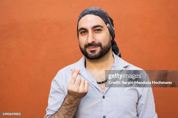 middle eastern, latino man with a bandana smiling, looking at the camera and making a korean heart gesture with his index finger and thumb, love - index finger fotografías e imágenes de stock