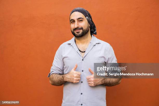 middle eastern, latino man with a bandana looking at the camera and giving a thumbs up - online voting stock pictures, royalty-free photos & images
