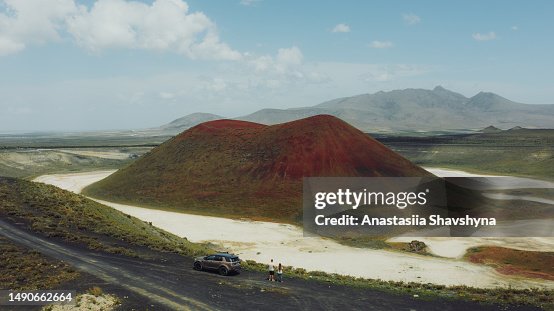 Aerial view of woman and man with a car on top of hill looking at the red volcano crater