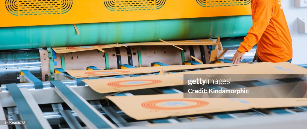 Automatische Maschine zum Schneiden und Drucken von Kartons in Betrieb, Indoor-Lagerfabrik. Logistikverpackungsindustrie Geschäft, Industriejob oder Menschen bei der Arbeit Konzept