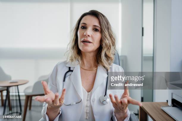 portrait of a female doctor talking to the camera in online care - camera stock pictures, royalty-free photos & images
