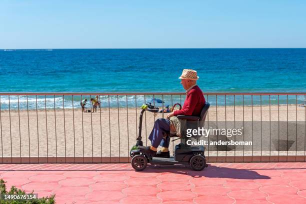 alone man sits in  one motorized chair and looking out over the sea in the city of benidorm in spain - motor cart stock pictures, royalty-free photos & images