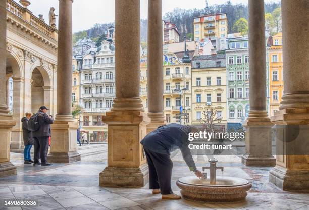 älterer mann, der seine tasse mit heißem quellwasser aus einem öffentlichen mittelalterlichen brunnen füllt - kolonnade stock-fotos und bilder