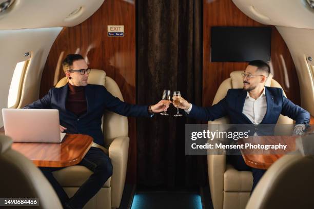 elegant smiling business couple in private jet airplane drinking champagne during the flight - first class champagne stock pictures, royalty-free photos & images