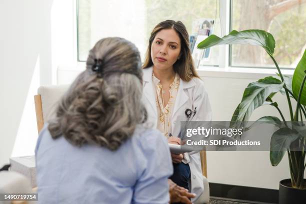 serious female doctor listens to unrecognizable female patient - gynaecoloog stockfoto's en -beelden