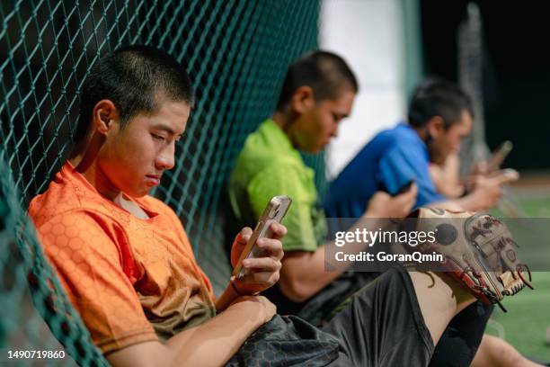 baseball players concentrated watching tutorials on mobile device in the batting cage at night - baseball cage stock pictures, royalty-free photos & images