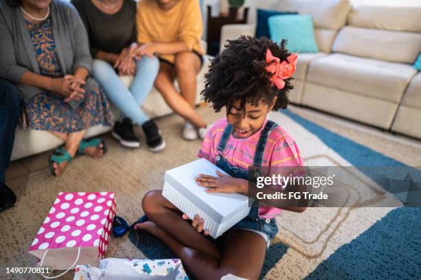 mädchen öffnet ein geschenk an ihrem geburtstag zu hause - geburtstagsgeschenk stock-fotos und bilder