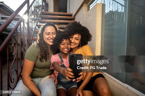 Girl child taking a selfie with her mothers using a mobile phone on house stairs Girl child taking a selfie with her mothers using a mobile phone on house stairs