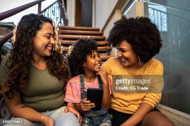 child girl having fun with her mothers using mobile phone sitting on house steps outdoors - adoption stockfoto's en -beelden