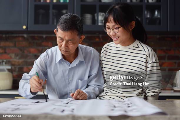 un grand-père asiatique est vu enseignant et montrant ses compétences en calligraphie à sa petite-fille à la maison. l’atmosphère est remplie de chaleur et d’amour alors que les membres de la famille s’engagent ensemble dans cette activité trad - écriture chinoise photos et images de collection