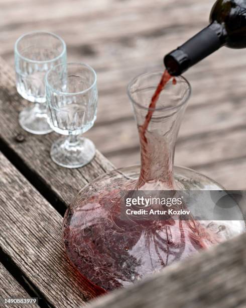 pouring red wine from bottle into decanter, two empty glasses on wooden table. glass smooth transparent decanter. aged gray wood background. wine tasting. close-up. top view. copy space. soft focus - french stock pictures, royalty-free photos & images