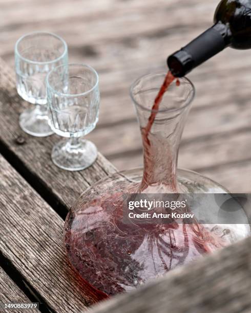 pouring red wine from bottle into decanter, two empty glasses on wooden table. glass smooth transparent decanter. aged gray wood background. wine tasting. close-up. top view. copy space. soft focus - bordeaux wine - fotografias e filmes do acervo