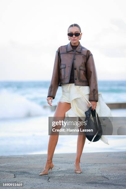 Guest wearing brown leather jacket, black Bottega Veneta bag and white skirt at Afterpay Australian Fashion Week 2023 at Carriageworks on May 17,...
