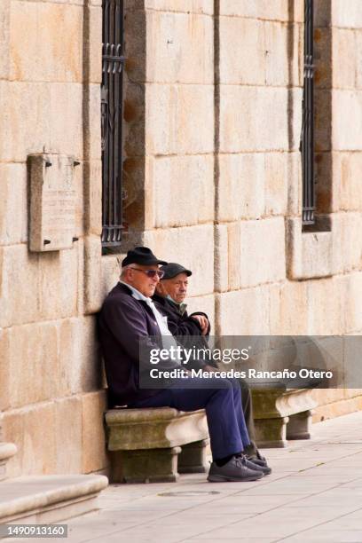hombres mayores sentados en un banco de piedra en la plaza del pueblo. - banco de españa fotografías e imágenes de stock