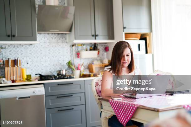 台所のテーブルでノートパソコンで作業する女性 - 感情表現シリーズ ストックフォトと画像