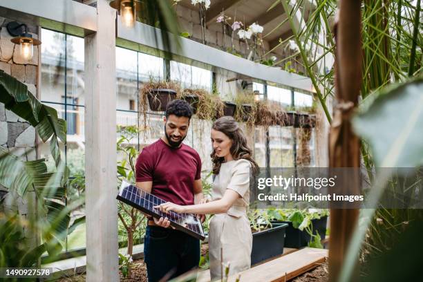 young couple in greenhouse with solar panel. - green economy stockfoto's en -beelden