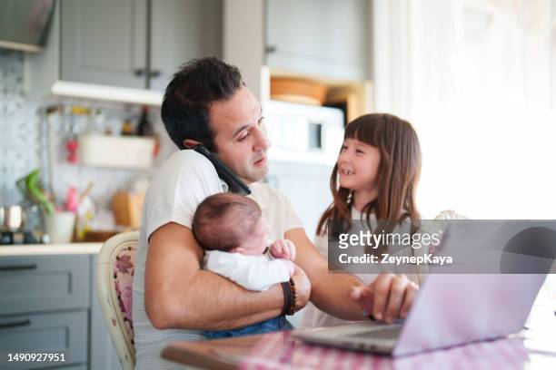 padre trabajando en una computadora portátil con sus dos hijos en la cocina - intergénero fotografías e imágenes de stock