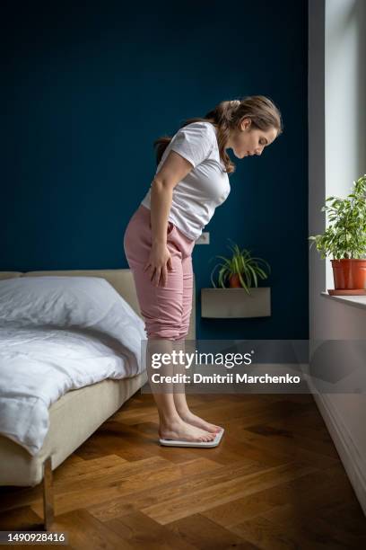 young overweight woman standing on weight scale in bedroom looking at data number on screen. - woman weight scale stock pictures, royalty-free photos & images