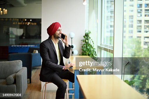 Sikh Indian man in formal wear speaking on the mobile phone near a window in a co- working space Sikh Indian man in formal wear speaking on the mobile phone near a window in a co- working space