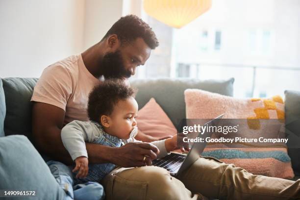 dad working on a laptop while sitting with his little son on a sofa - baby pointing stockfoto's en -beelden