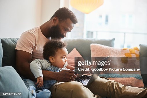 Dad working on a laptop while sitting with his little son on a sofa