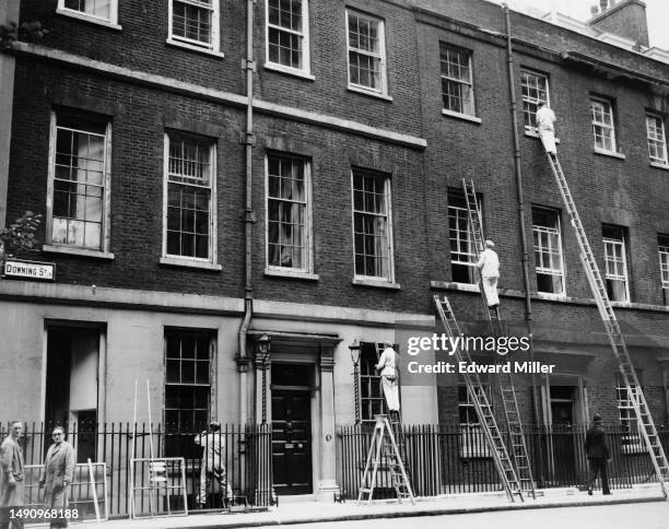 Labourers using ladders to paint the window frames of properties on Downing Street, off Whitehall in London, England, 8th September 1954. No 10...