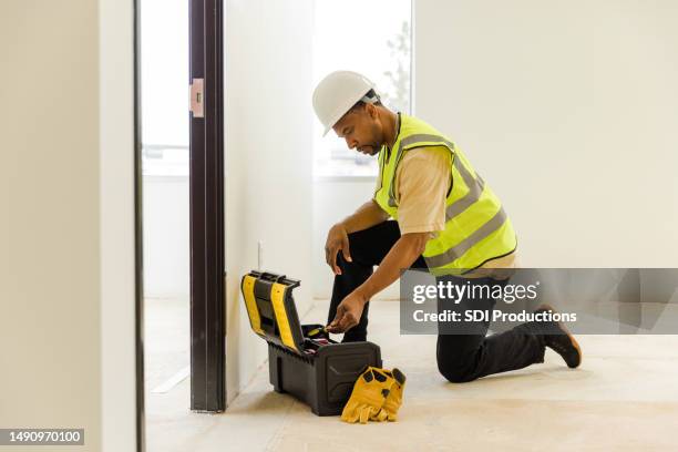 male electrician kneels down to look for tools to fix issues at the job site - flooring contractor stock pictures, royalty-free photos & images