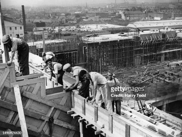 Labourers at work constructing the upper stands overlooking the swimming pool under construction at the Earls Court Exhibition Centre, in the Earl's...