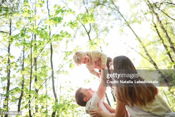 young family having fun in park, lifting their toddler son in air - affectionate mother stock pictures, royalty-free photos & images