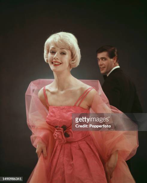 Posed studio portrait of a female fashion model wearing a pink evening dress with spaghetti straps and full skirt with a matching chiffon wrap, a man...