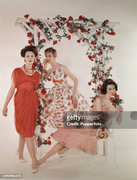 Posed studio portrait of three female fashion models wearing dresses in ruched and draped silk chiffon in shades of pink and rose print cotton, they...