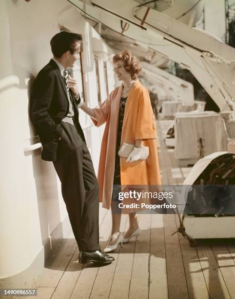 Vacation scene of a female fashion model talking to a man on the deck of a passenger liner, she wears an apricot swing style duster coat over a knee...