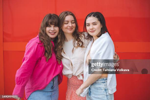 three attractive generation z ladies standing side by side in front of red background - größenunterschied stock-fotos und bilder