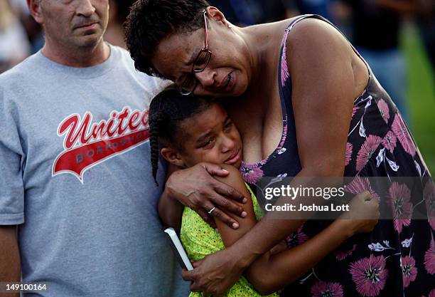 People pray and mourn during a memorial for the victims that were killed and wounded during the mass shooting at a movie theater last Friday, outside...