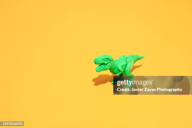 green plastic tyrannosaurus rex on yellow background - gigante personaggio fantastico foto e immagini stock