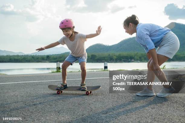 mother teaching her daughter how to skateboard in the park child riding skate board healthy sports,thailand - mother and daughter riding on skateboard in park stock pictures, royalty-free photos & images