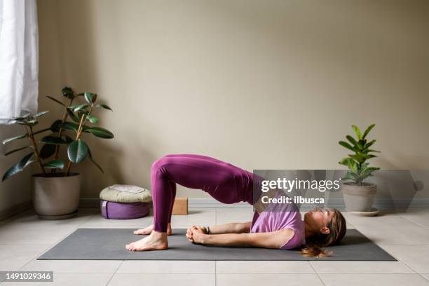 professional woman practicing yoga at home: bridge, setu bandha sarvangasana - setu bandha sarvangasana stock pictures, royalty-free photos & images