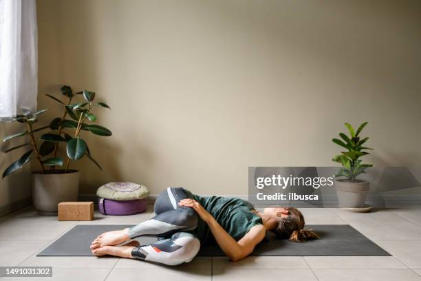 professional woman practicing yoga at home: supine spinal twist, supta matsyendrasana - lying on back stock pictures, royalty-free photos & images