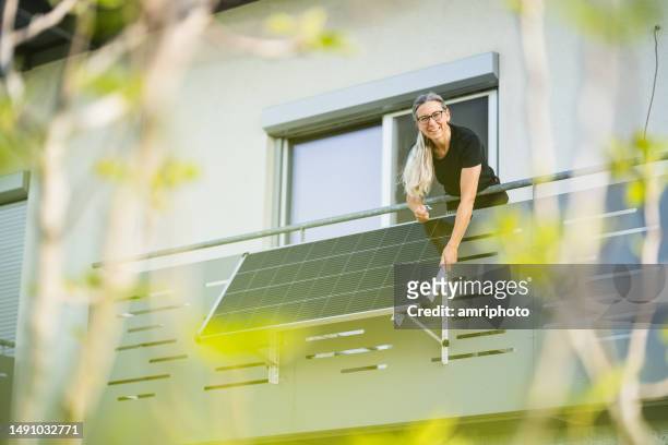 happy woman installing solar panel on houses balcony - zonnecellen stockfoto's en -beelden