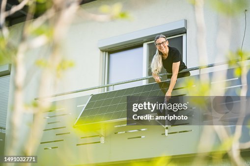 Happy woman installing solar panel on houses balcony Happy woman installing solar panel on houses balcony