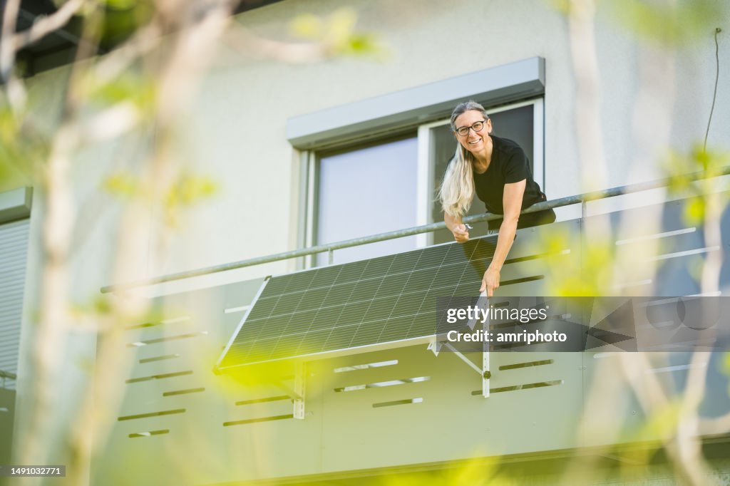 Happy woman installing solar panel on houses balcony