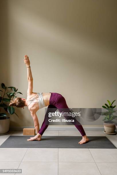 professional woman practicing yoga at home: revolved triangle, parivritta trikonasana - revolved triangle pose stock pictures, royalty-free photos & images