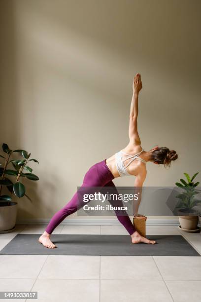 professional woman practicing yoga at home: revolved triangle, parivritta trikonasana - parivrtta trikonasana stock pictures, royalty-free photos & images