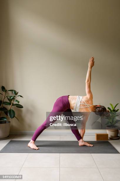 professional woman practicing yoga at home: revolved triangle, parivritta trikonasana - revolved triangle pose stock pictures, royalty-free photos & images